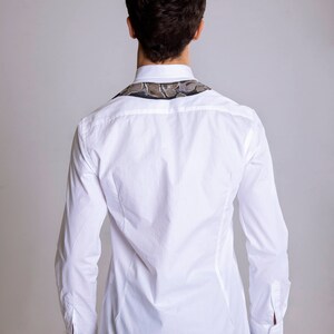 Peut inclure: Chemise blanche &agrave; manches longues avec un col &agrave; motifs. Le col pr&eacute;sente un motif dans les tons marron, gris et noir. La chemise est boutonn&eacute;e et a une coupe ajust&eacute;e, port&eacute;e avec un jean bleu.