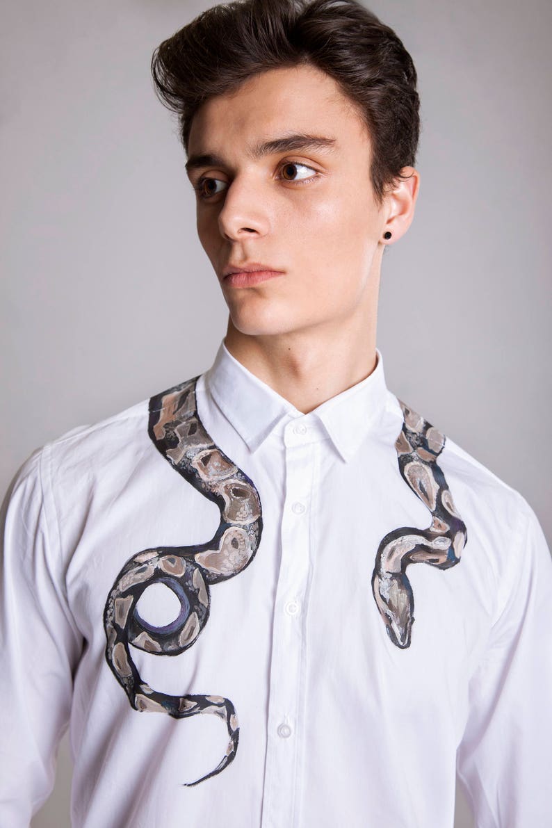 Peut inclure: Chemise blanche avec un motif de serpent peint &agrave; la main en nuances de marron, gris et noir. Le motif de serpent entoure le col et la poitrine, cr&eacute;ant un look unique et artistique. Un v&ecirc;tement de mode cr&eacute;atif et &eacute;l&eacute;gant.