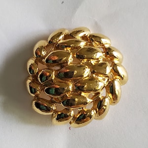 May include: A gold-toned metal button with a unique design of overlapping ovals. The button has a smooth, shiny finish.
