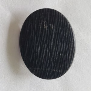 May include: A black round button with a textured surface.