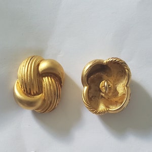 May include: Two gold-colored buttons, one with a knotted design and the other with a four-leaf clover design.