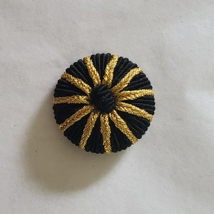 May include: A black and gold round button with a raised center and a starburst design.