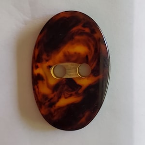 May include: A brown and orange oval-shaped button with two holes. The button has a marbled pattern.