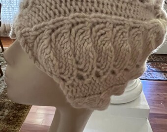 May include: A light beige knitted hat with a textured pattern. The hat is made of thick yarn and has a rounded crown. The hat is displayed on a mannequin head.