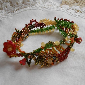 May include: A beaded bracelet with a floral design in shades of red, green, and gold. The bracelet is made with small, intricate beads and features a delicate flower design.