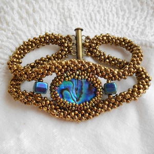 May include: A gold beaded bracelet with a blue abalone shell and blue glass beads. The bracelet has a toggle clasp.