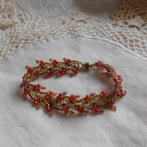 May include: A beaded bracelet with a gold and red color scheme. The bracelet is made with small beads and has a clasp closure.