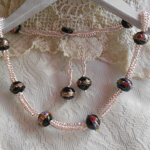 May include: A delicate necklace and earrings set featuring black glass beads with gold and colorful accents. The necklace is made with multiple strands of tiny seed beads.