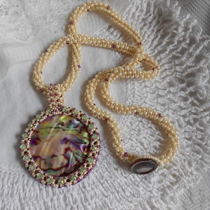May include: A pearl and abalone shell necklace with a round pendant. The pendant is surrounded by green and purple beads. The necklace is on a white crocheted surface.