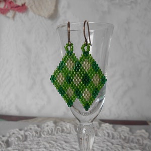 May include: A pair of green and white beaded earrings with a diamond shape. The earrings are hanging from a glass goblet.