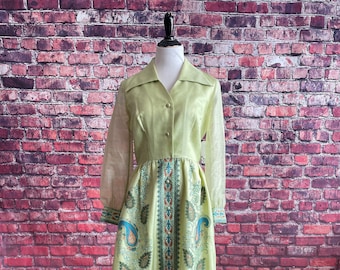 May include: A long, green dress with a paisley print. The dress has a collared neckline and long sleeves. The sleeves are sheer and the dress is made of a silky fabric.