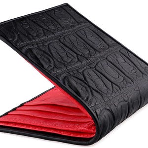 May include: Black leather wallet with a textured crocodile pattern on the exterior. The interior is a vibrant red, creating a striking contrast. The wallet is open, showcasing the interior lining.