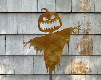 Może przedstawiać: Rdzawy metalowy straszak na Halloween z głową dyni i rozłożonymi ramionami. Straszak stoi przed szarą drewnianą ścianą.