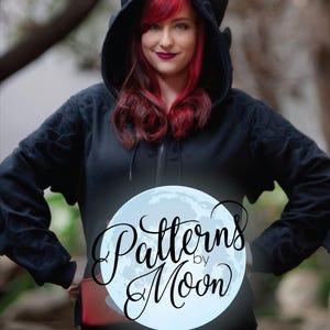 Könnte beinhalten: Schwarzer Kapuzenpullover mit einem von Drachen inspirierten Kapuze mit Hörnern und strukturierten Details. Der Hoodie hat einen Frontreißverschluss und eine rote Tasche. Der Text "Patterns by Moon" ist enthalten.