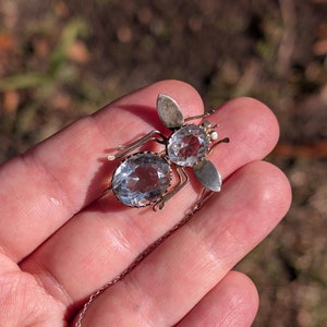 May include: A silver bee brooch with two clear faceted glass stones. The bee has a chain attached to the back with a safety pin.