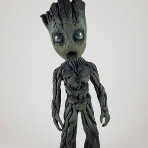 Könnte beinhalten: Eine handbemalte, schwarz-grüne Figur eines baumartigen Charakters mit einem humanoiden Körper und großen Augen. Die Figur steht auf einem weißen Hintergrund.