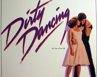 May include: A vintage vinyl record album cover for the movie Dirty Dancing, featuring Patrick Swayze and Jennifer Grey. The cover is white with a purple and red stylized title "Dirty Dancing" and the text "The Time of Your Life."