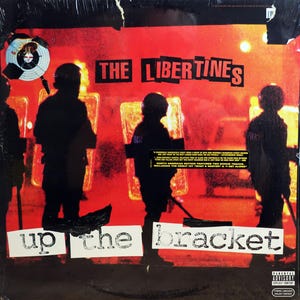 May include: Album cover for "Up the Bracket" by The Libertines. The cover features a red background with black silhouettes of figures and the band's name in bold black letters. The album title is in white block letters.