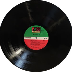 May include: Black vinyl record with a red, white and green label. The label has the text "Atlantic" in a white circle with a red "4" and a red "S" inside. The text "Bette Midler" is below the circle. The label also has the text "Stereo" and "One" in green. The track list includes "Skylark", "Drinking Again", "Breaking Up Somebody's Home", "Surabaya Johnny", and "I Shall Be Released".