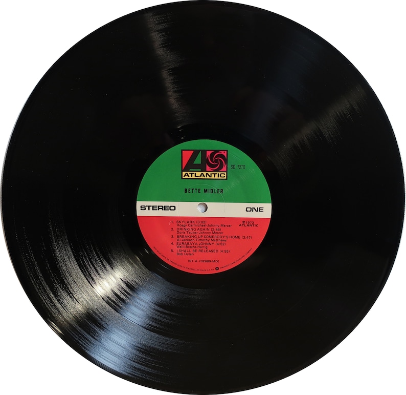 May include: Black vinyl record with a red, white and green label. The label has the text "Atlantic" in a white circle with a red "4" and a red "S" inside. The text "Bette Midler" is below the circle. The label also has the text "Stereo" and "One" in green. The track list includes "Skylark", "Drinking Again", "Breaking Up Somebody's Home", "Surabaya Johnny", and "I Shall Be Released".