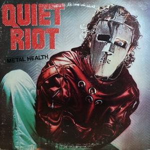 May include: A red leather jacket with a metal mask on the person wearing it. The jacket has several small buttons with images of people on them. The text "Quiet Riot" and "Metal Health" is visible on the album cover.