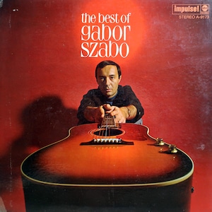 Peut inclure: Pochette d'album pour "The Best of Gabor Szabo" avec un homme tenant une guitare acoustique. La couverture a un fond rouge et du texte blanc. Le logo Impulse! Records est dans le coin supérieur droit.