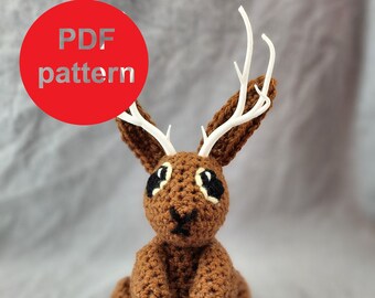 May include: A brown crocheted rabbit with white antlers. The rabbit is sitting with its legs crossed. The image includes the text "PDF pattern" and "Step by step instructions".