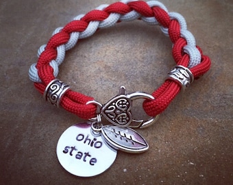 May include: Red and gray braided bracelet with a silver charm that says "Ohio State" and a football charm.