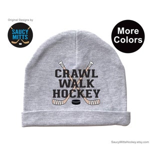 May include: Gray beanie with the text "Crawl Walk Hockey" and a graphic of two crossed hockey sticks and a puck.