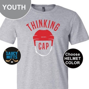 May include: Gray youth t-shirt with the text "Thinking Cap" and a hockey helmet graphic. The helmet is red. The text "Choose Helmet Color" is on a black circle. The text "Saucy Mitts" is on a blue circle with a hockey stick graphic.