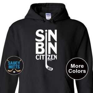 May include: Black hoodie with white text that reads "SIN BIN CITIZEN" with a hockey stick graphic. The hoodie has a pocket on the front and is available in other colors.