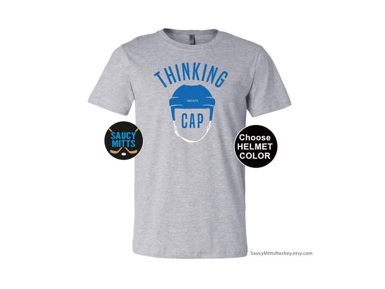 May include: Gray t-shirt with the text "Thinking Cap" and a blue hockey helmet graphic. The shirt also has two small logos, one that says "Saucy Mitts" and another that says "Choose Helmet Color".