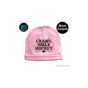 May include: Pink baby beanie with the text "Crawl Walk Hockey" and a hockey stick graphic.