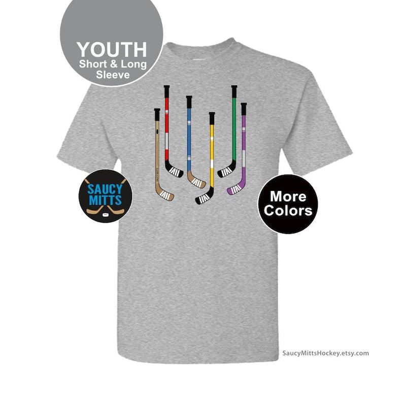Op de afbeelding: Grijs T-shirt voor jeugd met een ontwerp van hockeysticks in verschillende kleuren. De tekst "Saucy Mitts" en "Meer kleuren" staat op het T-shirt.