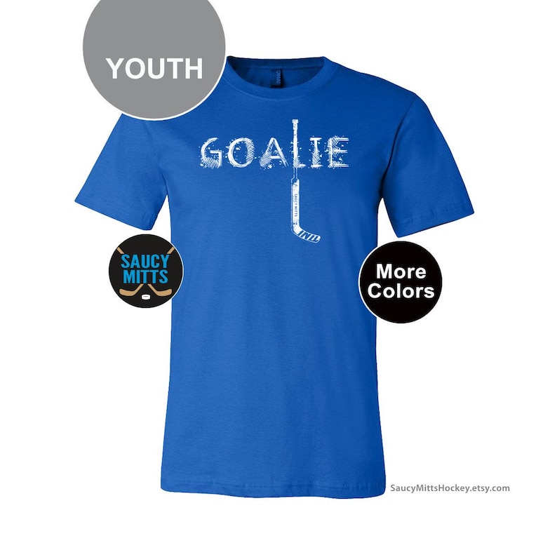 Op de afbeelding: Koningsblauw t-shirt met het woord "GOALIE" in het wit, met een hockey stick graphic. Het shirt heeft een ronde hals en korte mouwen. Het woord "YOUTH" staat in een grijze cirkel linksboven.