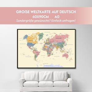 May include: A framed world map with detailed country borders, cities, and geographical features. The map is 60x90cm and is displayed above a white sofa. Text on the map reads "GROBE WELTKARTE AUF DEUTSCH".