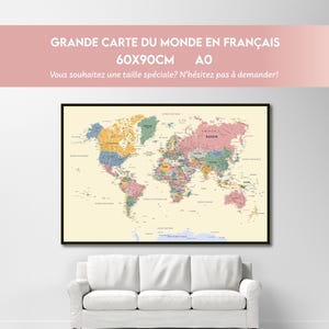 Può includere: Una mappa del mondo incorniciata in una cornice nera, esposta sopra un divano bianco. La mappa è una rappresentazione dettagliata e colorata del mondo, con testo in francese. La mappa misura 60x90cm.