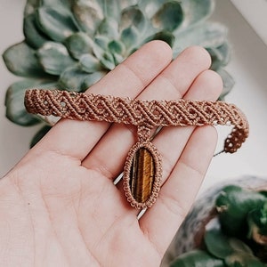 May include: A brown macrame choker necklace with a tiger's eye stone pendant.