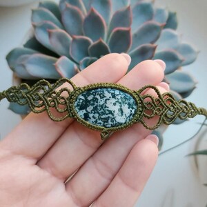May include: A green and white agate stone is set in a green macrame bracelet. The bracelet is made with a knotted cord and has a decorative design.