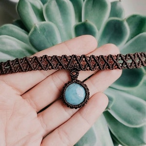 May include: A brown macrame choker necklace with a light blue gemstone pendant.
