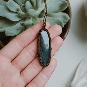 May include: A dark blue oval labradorite gemstone pendant on a brown cord necklace.