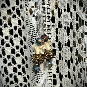 K&ouml;nnte beinhalten: Ein Paar Ohrringe mit einem knochenf&ouml;rmigen Anh&auml;nger und bunten Emailleperlen. Die Perlen sind blau, gr&uuml;n, rot und wei&szlig;.