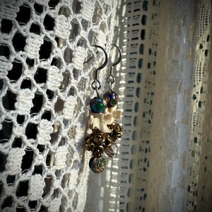 K&ouml;nnte beinhalten: Ein Paar Ohrringe mit einem wei&szlig;en knochenartigen Anh&auml;nger, blauen und gr&uuml;nen Emailleperlen und goldfarbenen Akzenten.