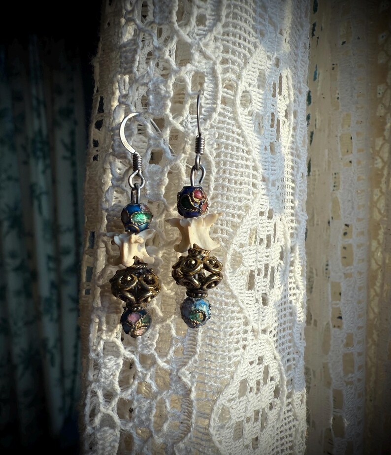 K&ouml;nnte beinhalten: Ein Paar silberne Ohrringe mit knochenf&ouml;rmigen Anh&auml;ngern, mehrfarbigen Glasperlen und verzierten Metallakzenten.