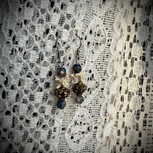 K&ouml;nnte beinhalten: Ein Paar Ohrringe mit wei&szlig;en knochenartigen Anh&auml;ngern, goldenen Perlen und blauen und wei&szlig;en gemusterten Glasperlen.