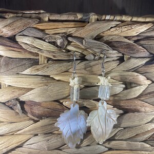 Op de afbeelding: Een paar zilveren oorbellen met witte schelpbladeren en heldere glazen kralen.