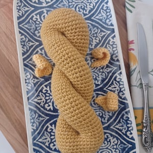 Może przedstawiać: Plecione, żółte bułeczka zrobiona na szydełku na talerzu z niebiesko-białym wzorem. Bułeczka ma kształt precla.