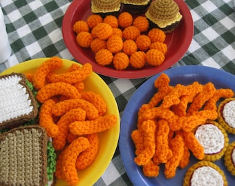 May include: A close-up of crocheted food items on plates. There are crocheted sandwiches, french fries, chicken nuggets, and pizza slices. The plates are yellow, red, and blue.
