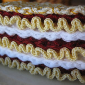 May include: A crocheted cake made with white, red, and yellow yarn. The cake is layered and has a scalloped edge.