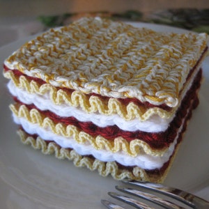 May include: A crocheted lasagna dish made with yellow, white, and red yarn. The dish is layered and has a realistic appearance.